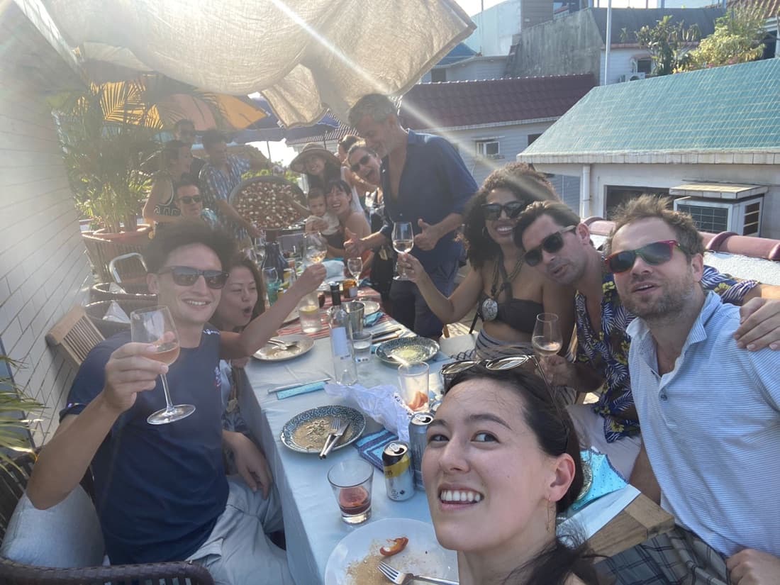 Friends raising glasses around a long rooftop dinner table in the evening sun