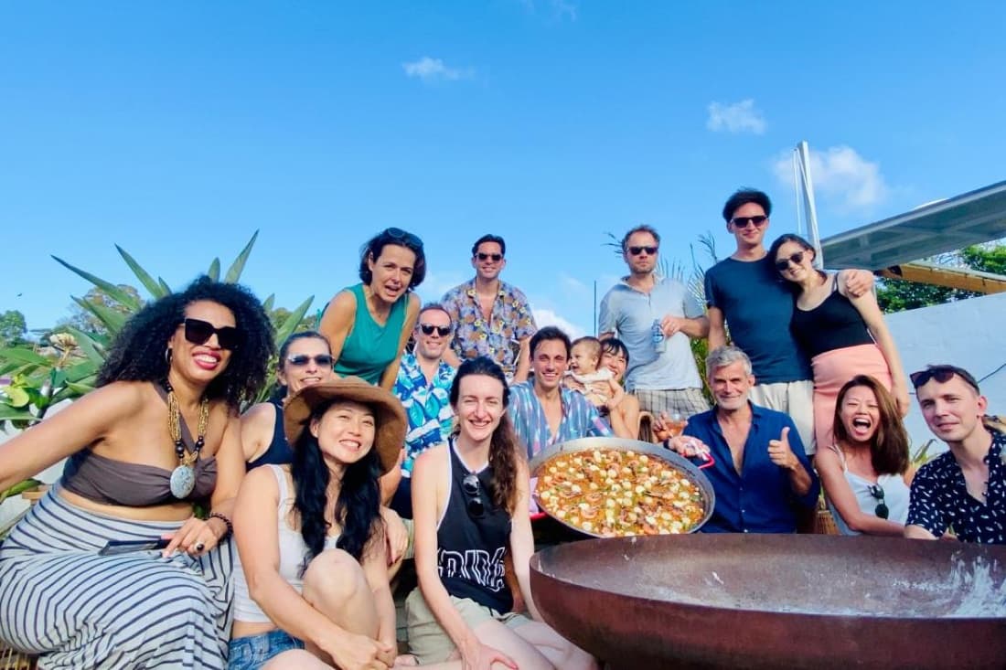 A big group of friends posing behind a fresh paella on a sunny terrace